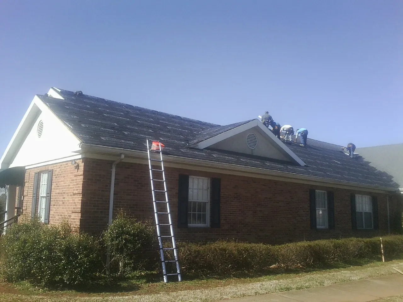 Crew tearing shingles off a brick ranch roof with a ladder set — Emergency Roof Repair work by our crew in Pelion