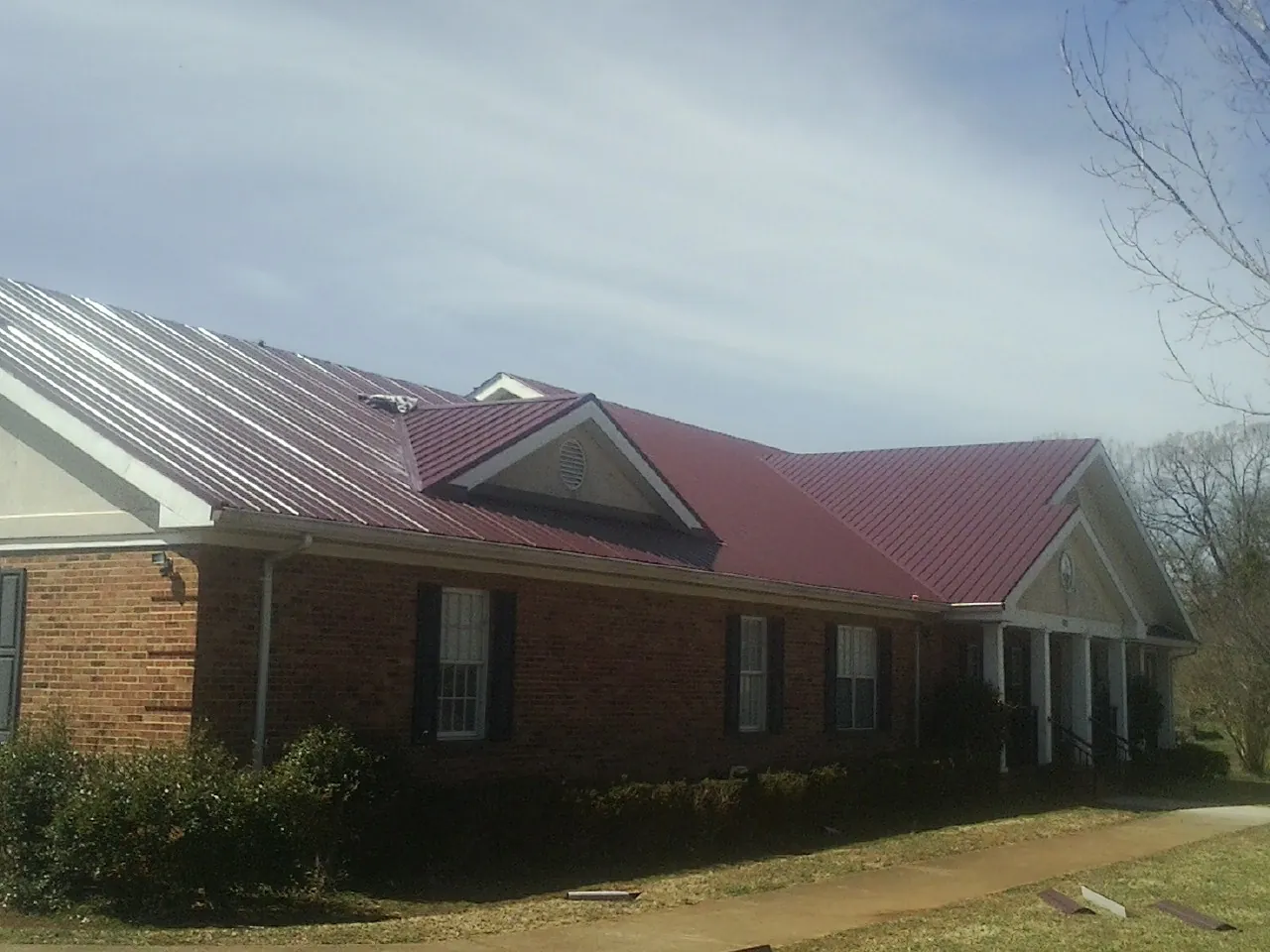 Red metal roof with gabled entries on a long brick building, from a Hail Damage Roof Repair job in Pelion