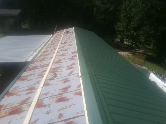 Old rusted panels beside newly installed green metal roofing — Wind Damage Roof Repair by Roofing Brothers in Pelion