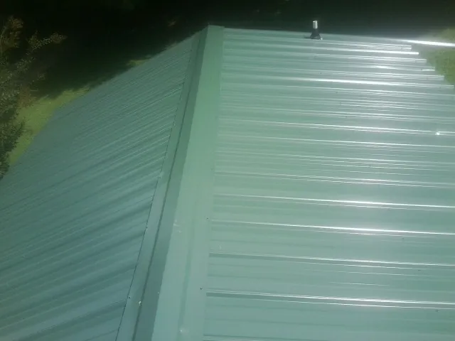 New green metal panels meeting at the ridge of a roof — Flat Roof Repair work by our crew in Pelion