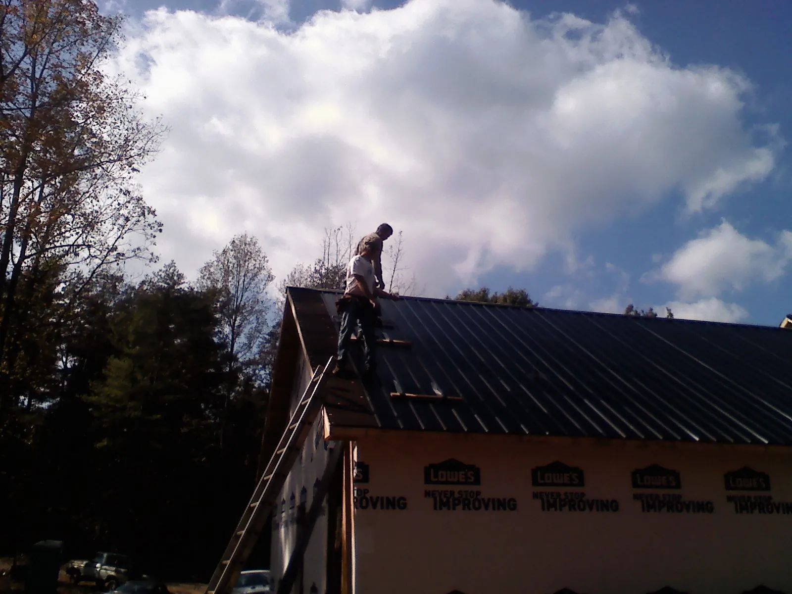 Roofer fastening dark metal panels high against a cloudy sky, from a Roof Inspection job in Pelion