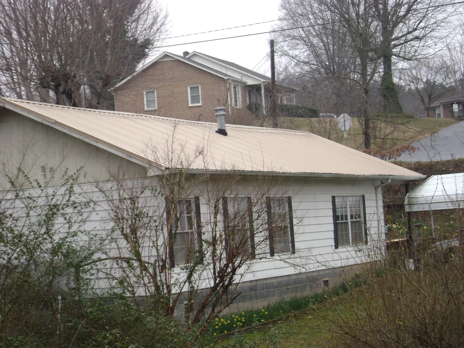 Tan metal roof on a white sided house set into a hillside — Commercial Roofing by Roofing Brothers in Pelion