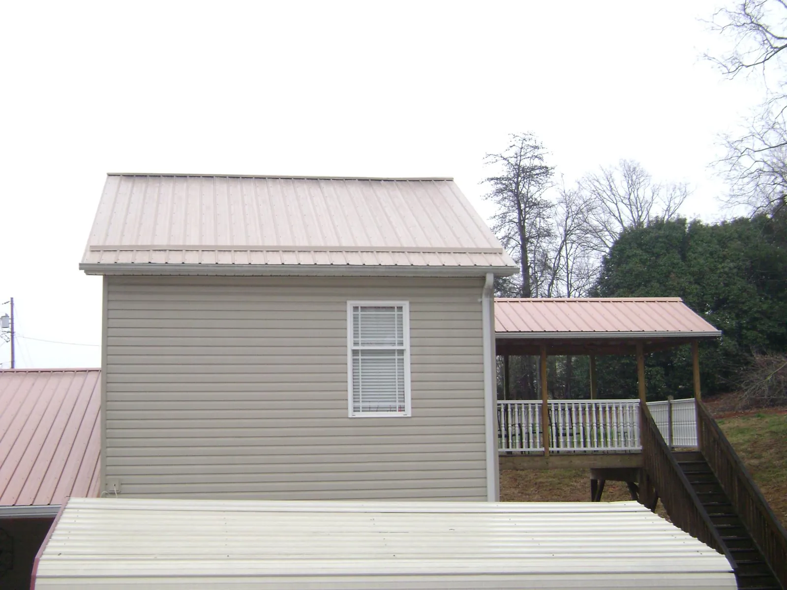 Tan metal roofs on a two story addition and attached porch, from a Roof Replacement job in Pelion